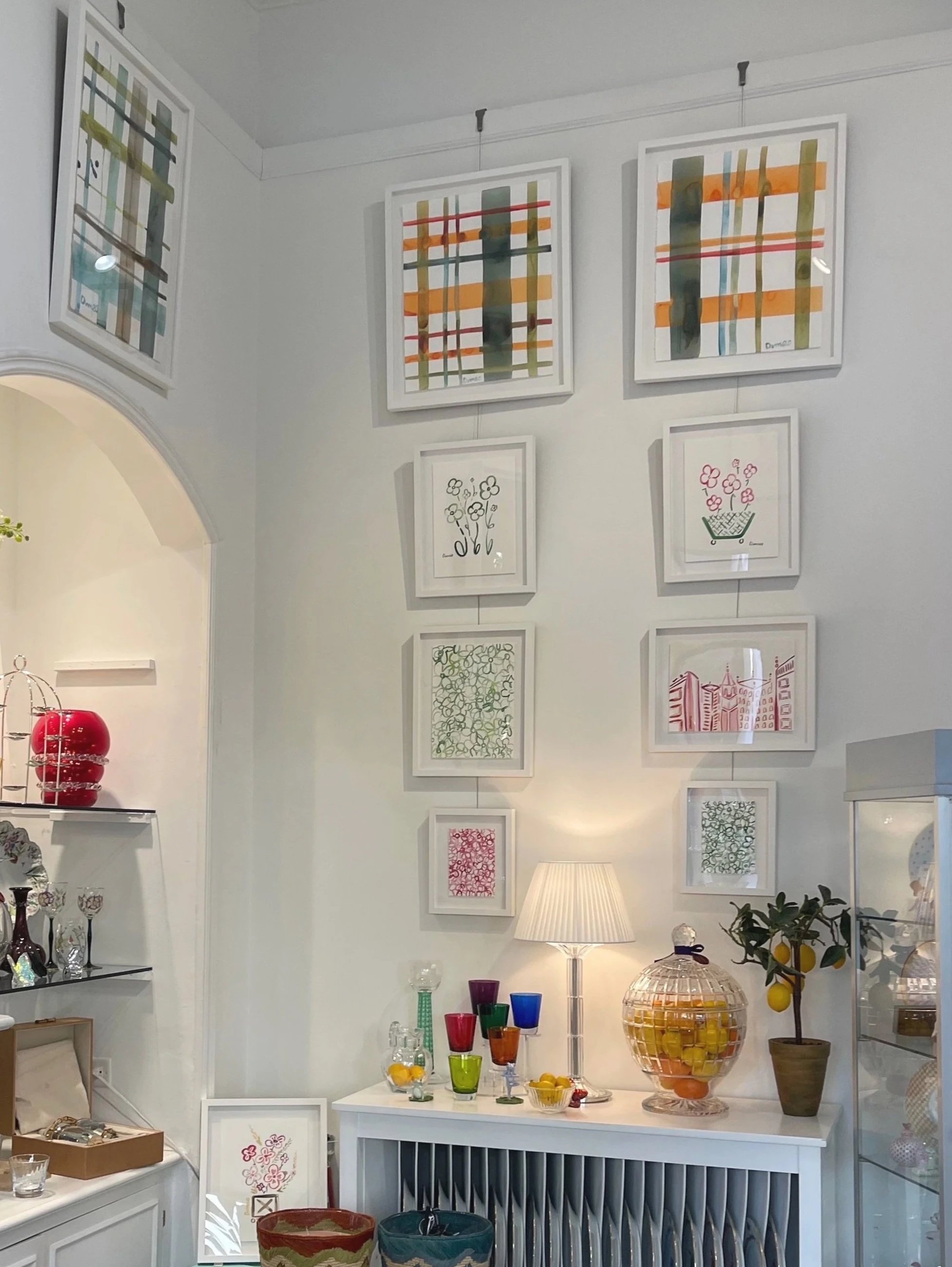 Framed paintings by Molly Dimeo displayed above glassware at Mary Mahoney in Palm Beach.